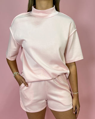 Person wearing a pink outfit with a matching top and shorts on a pink background
