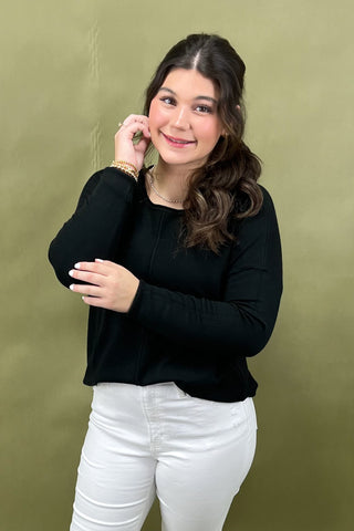 Woman wearing a black top and white pants against an olive green background