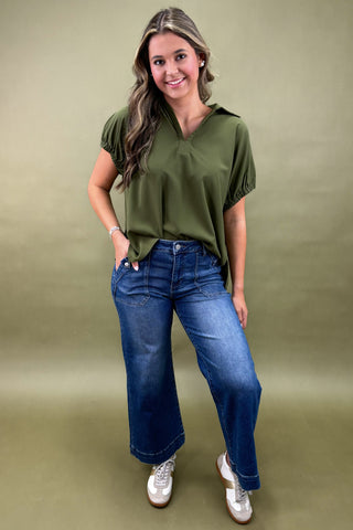 Woman wearing a green top and blue jeans against a green background