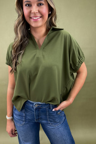 Woman wearing an olive green top and blue jeans against a beige background