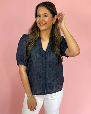Woman wearing a navy lace blouse against a pink background