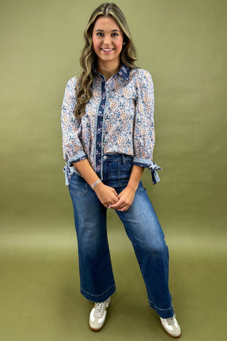 Woman wearing a patterned blouse and blue jeans on a green background