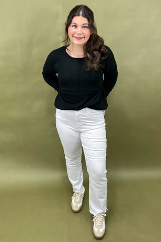 Person wearing a black top and white pants against a green background