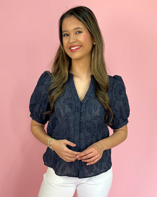 Woman wearing a navy blue lace blouse against a pink background