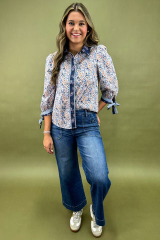 Woman wearing a floral blouse and blue jeans against a green background