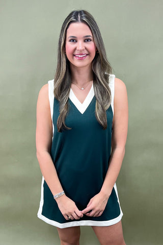 Woman wearing a green dress with white trim against a plain background