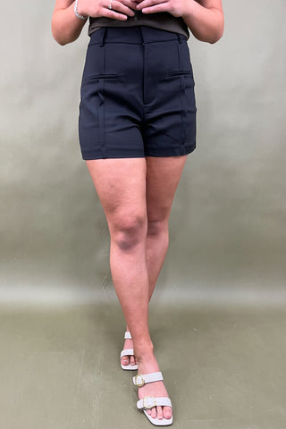 Person wearing black shorts and white sandals on a plain background