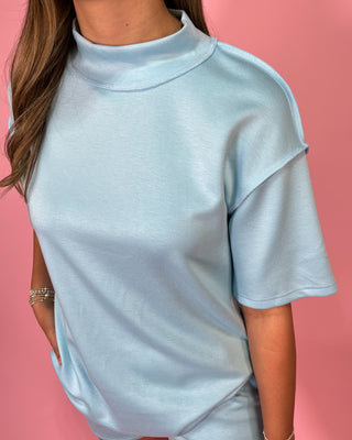 Light blue top worn by a person on a pink background