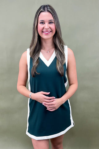 Woman wearing a green dress with white trim against a plain background