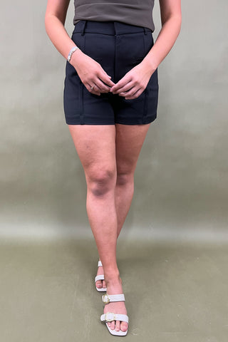 Person wearing black shorts and white sandals on a plain background