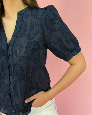 Navy lace blouse worn by a person on a pink background