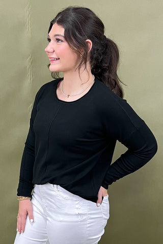 Woman wearing a black long-sleeve top and white pants against a green background