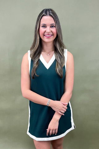 Woman wearing a green dress with white trim against a plain background