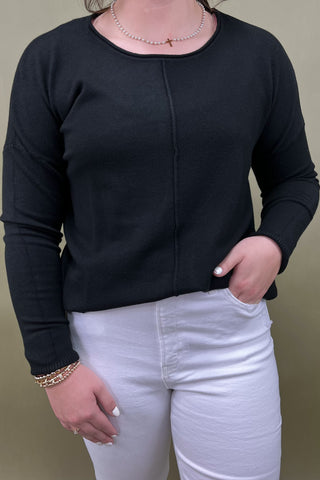 Person wearing a black long-sleeve top and white pants against a neutral background