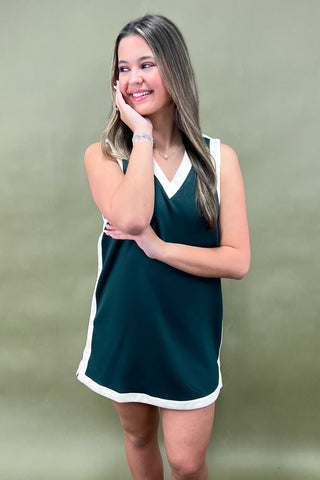Woman wearing a green dress with white trim against a plain background