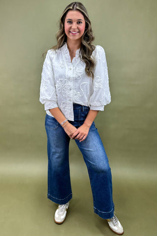 Woman wearing a white embroidered blouse and blue jeans against a green background
