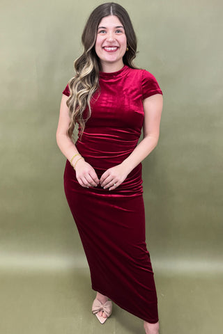 Woman wearing a burgundy velvet dress against a green background