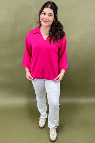 Woman wearing a bright pink blouse and white pants against a green background