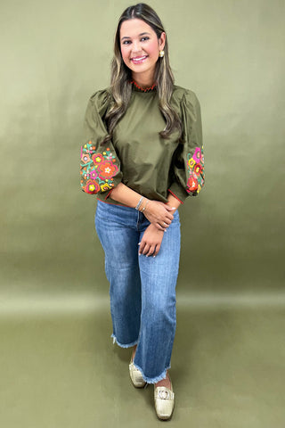 Woman wearing a green blouse with floral cuffs and sleeves against a green background
