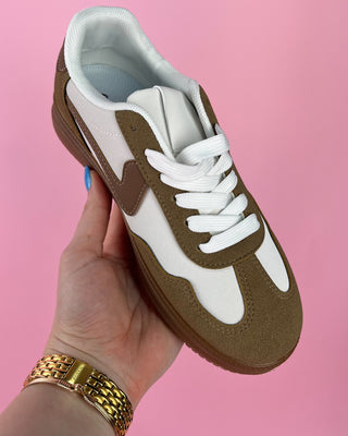 Brown and white sneaker held in a hand against a pink background