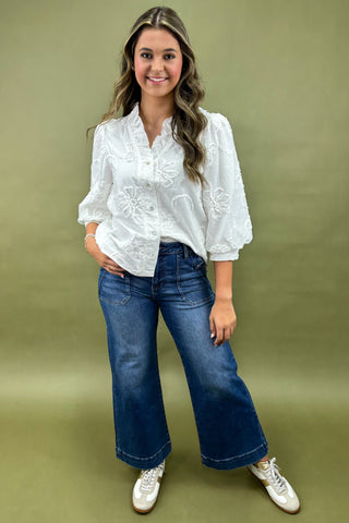 Woman wearing a white blouse with floral embroidery and blue jeans on a green background