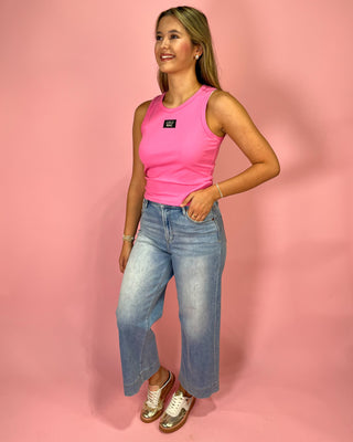 Woman wearing a pink tank top and blue jeans against a pink background