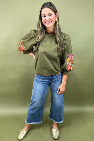 Woman wearing an olive green top with floral sleeves against a green background