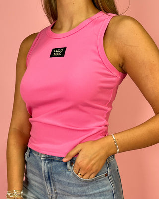 Person wearing a pink tank top with a visible brand logo against a pink background