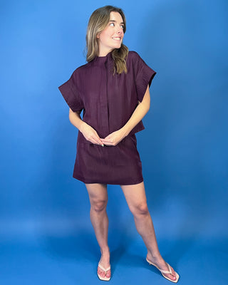 Burgundy two-piece skirt set featuring a relaxed short-sleeve top with a high neckline and a coordinating structured mini skirt.