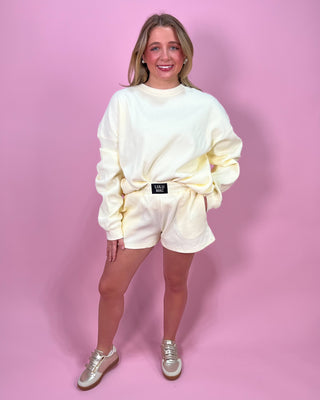 Person wearing a cream-colored sweatshirt and shorts set on a pink background