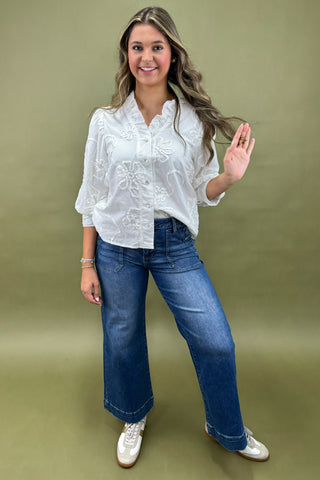 Woman wearing a white embroidered blouse and blue jeans on a green background