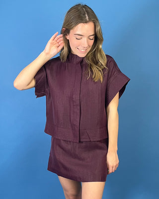 Burgundy two-piece skirt set featuring a relaxed short-sleeve top with a high neckline and a coordinating structured mini skirt.