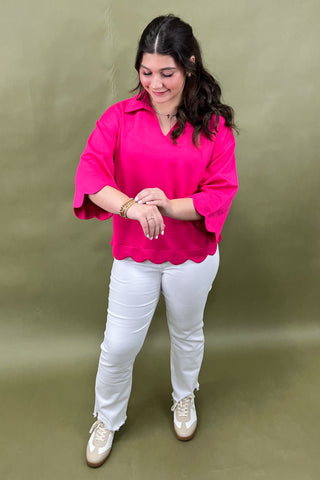 Woman wearing a bright pink blouse and white pants against a green background