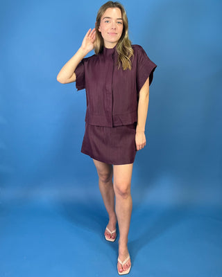 Burgundy two-piece skirt set featuring a relaxed short-sleeve top with a high neckline and a coordinating structured mini skirt.