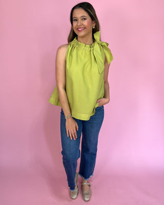 Woman wearing a green top with ruffled sleeves against a pink background