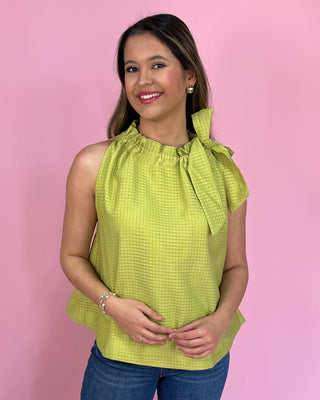 Woman wearing a green sleeveless top with a bow detail against a pink background