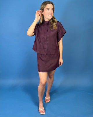 Burgundy two-piece skirt set featuring a relaxed short-sleeve top with a high neckline and a coordinating structured mini skirt.
