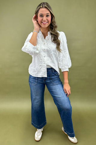 Woman wearing a white blouse and blue jeans against a green background