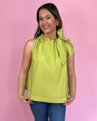 Woman wearing a green sleeveless top with a bow detail against a pink background