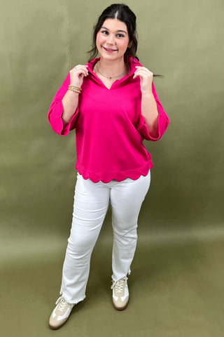 Woman wearing a bright pink top and white pants against a green background