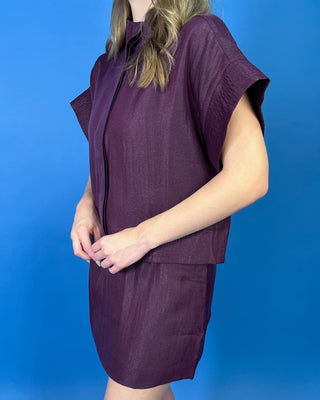 Burgundy two-piece skirt set featuring a relaxed short-sleeve top with a high neckline and a coordinating structured mini skirt.