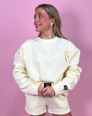 Person wearing a cream-colored sweatshirt and shorts with visible branding on a pink background