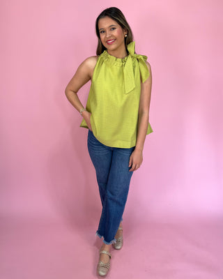 Woman wearing a green top with a bow and blue jeans against a pink background