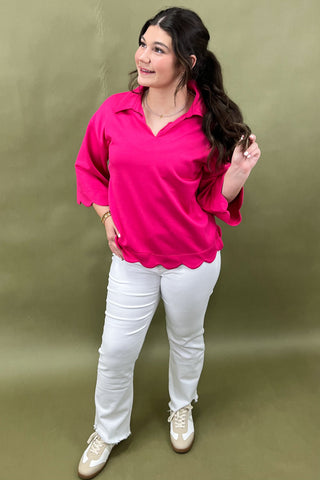 Woman wearing a bright pink top and white pants against a green background