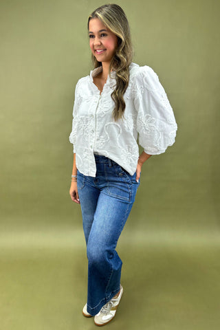 Woman wearing a white blouse with lace details and blue jeans on a green background