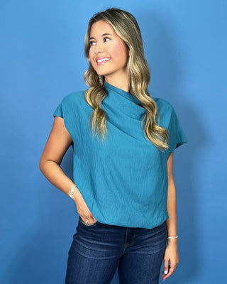 a teal short-sleeve draped top and dark blue jeans