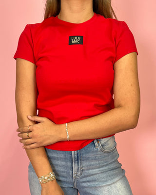 Person wearing a red t-shirt with a small logo on a pink background