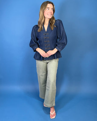 Dark wash denim peplum top featuring a notched neckline, puff sleeves, statement knotted front closures, and a flattering fitted waist.