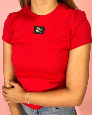 Person wearing a red t-shirt with a LULU MAC logo on a pink background