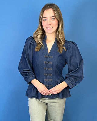 Dark wash denim peplum top featuring a notched neckline, puff sleeves, statement knotted front closures, and a flattering fitted waist.